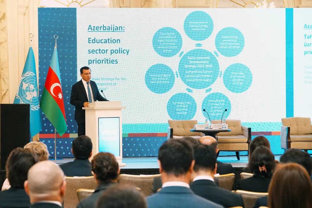 A government representative speaks at the podium during the 7th SDG Dialogue in Baku, with UN and Azerbaijan flags and an education strategy slide projected on screen.