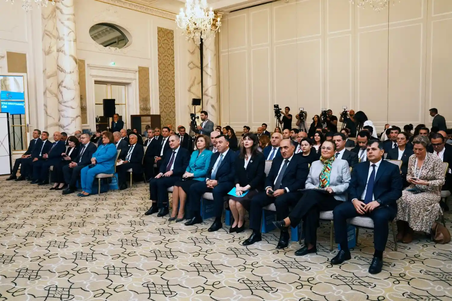 High-level participants and government officials attend the 7th SDG Dialogue in Baku, seated in a formal conference hall with press coverage in the background.