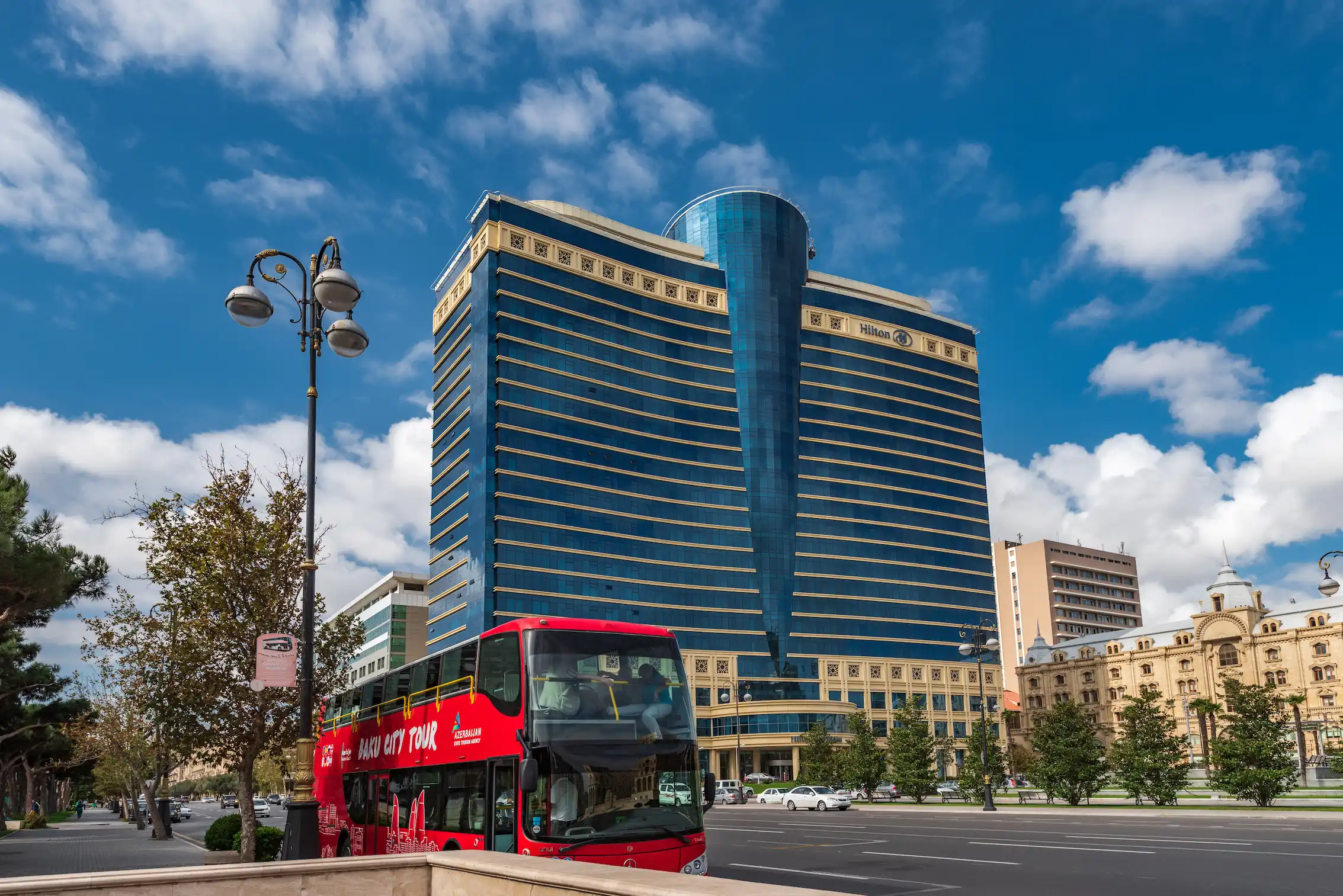 Red double-decker Mercedes-Benz Baku City Tour Bus starts its city tour at the Hilton Hotel near the Caspian Sea.