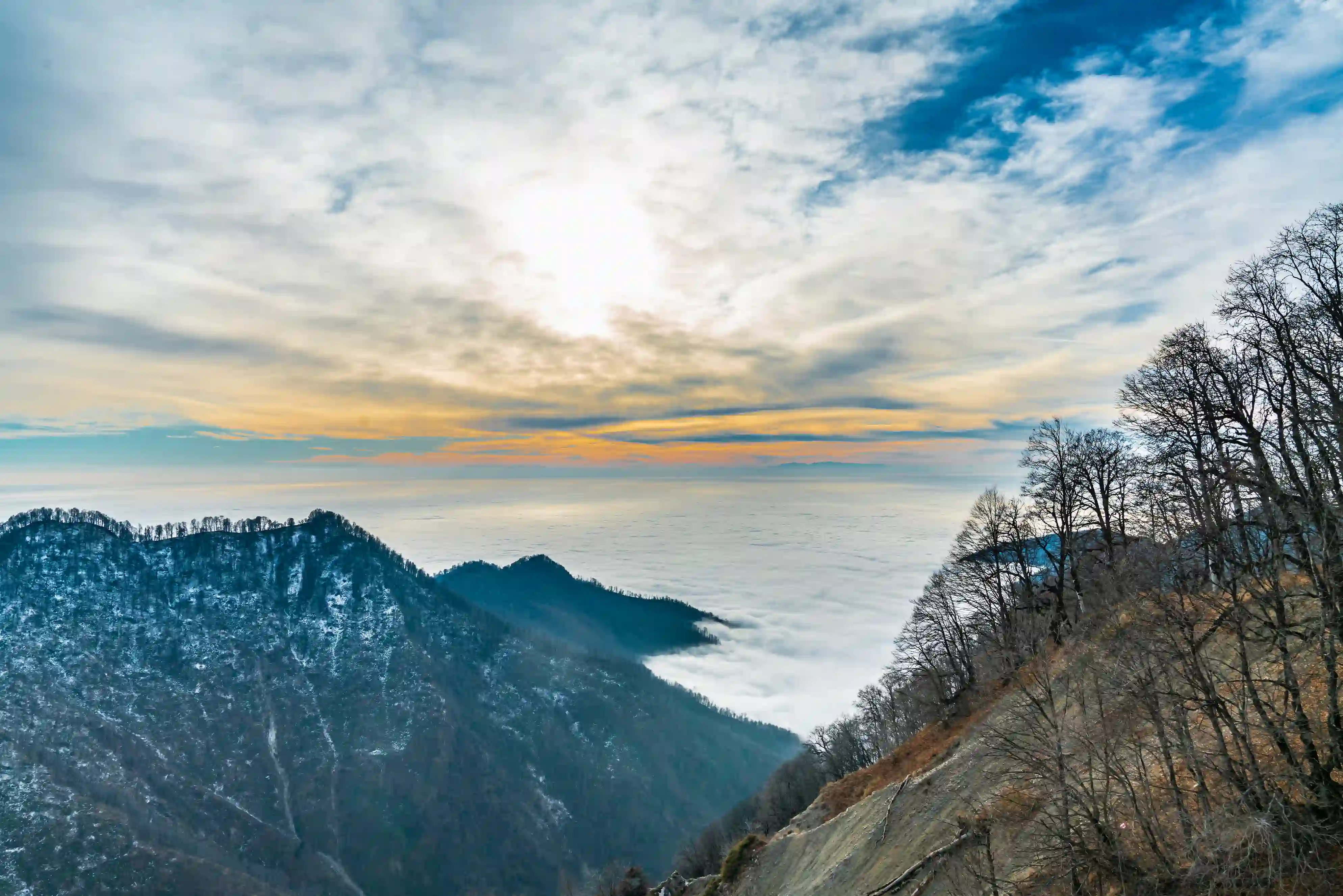 A stunning sunset view from the Gabala Cable Car captures snow-covered mountains and misty valleys under a glowing orange and blue sky.